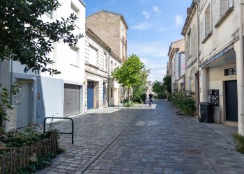 Vue d'une rue pavé avec des arbres sur les côtés et un cycliste roulant dessus. 