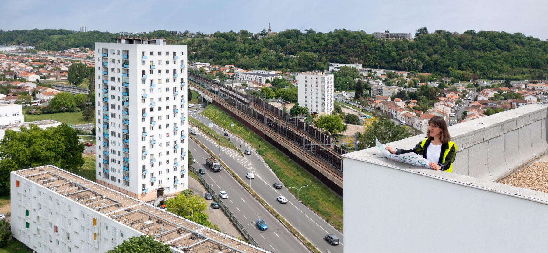 Responsable de rénovation urbaine en haut d'une tour avec une carte dépliée du quartier regarde les immeubles alentours