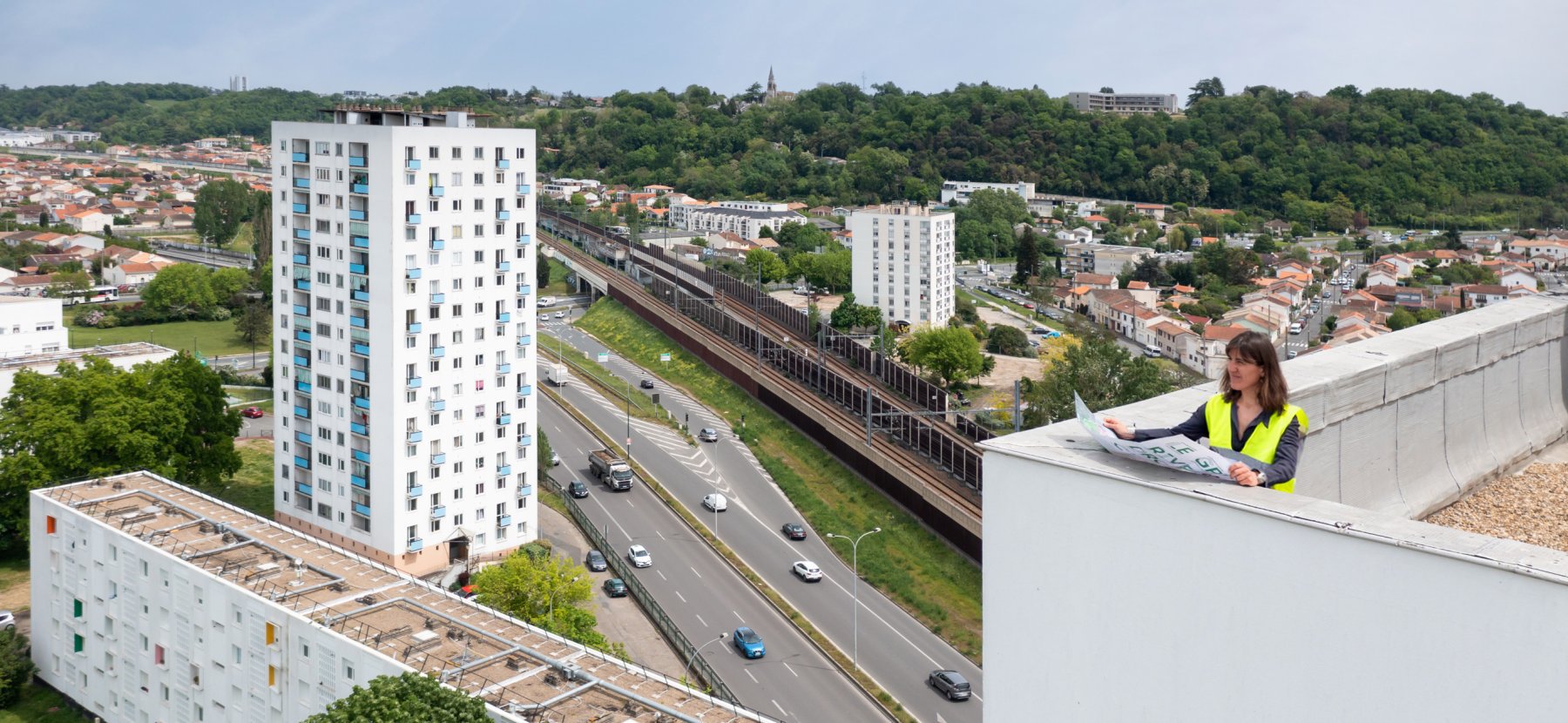 Responsable de rénovation urbaine en haut d'une tour avec une carte dépliée du quartier regarde les immeubles alentours