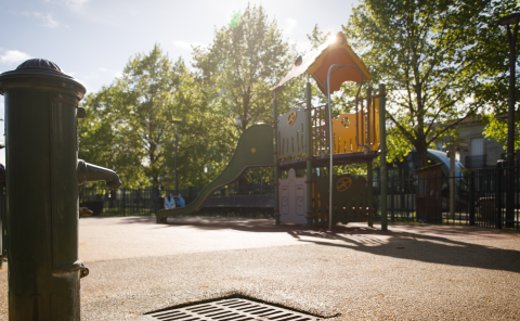 Un parc au second plan avec des arbres et de l'ombre. Un robinet public au premier plan.
