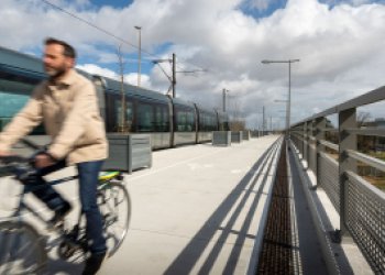 Piste cyclable menant à l'aéroport suivant la voie du tram avec un cycliste et un tram côté à côte