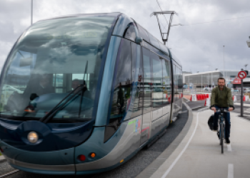 Vue du tram arrivant de l'aéroport avec un cycliste qui roule à côté.