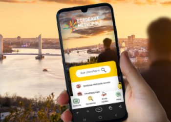 Un smartphone avec a page d'accueil de bordeaux-metropole.fr devant le paysage