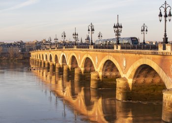 Visuel du pont de pierre avec un tram, et en fond de plan la rive gauche