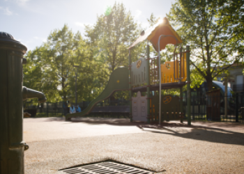 Un parc au second plan avec des arbres et de l'ombre. Un robinet public au premier plan.