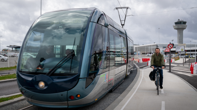 Vue du tram arrivant de l'aéroport avec un cycliste qui roule à côté.