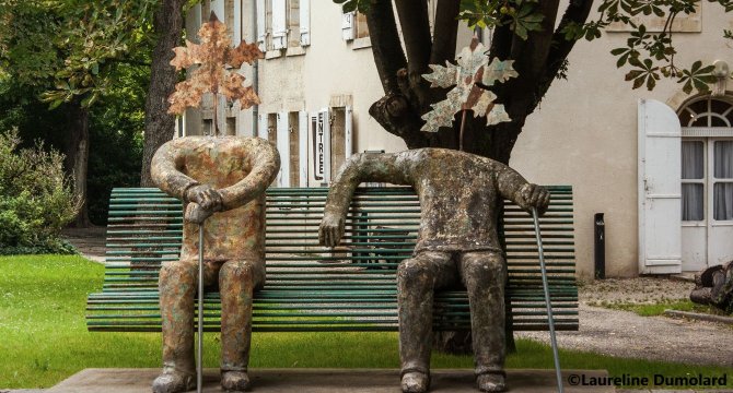 Les deux papis sculptés assis sur un banc avant restauration. Ils sont sombres et sans couleurs