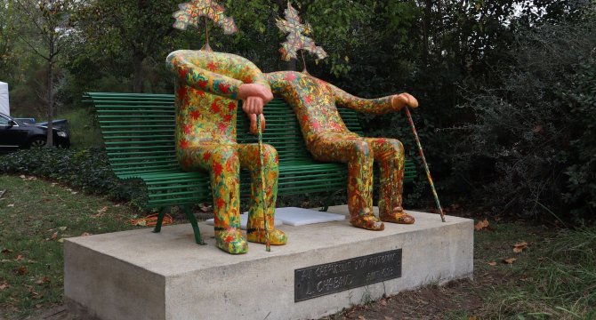 Les deux papis sculptés assis sur un banc après restauration. Ils ont plein de couleurs rouges vertes en mosaiques.