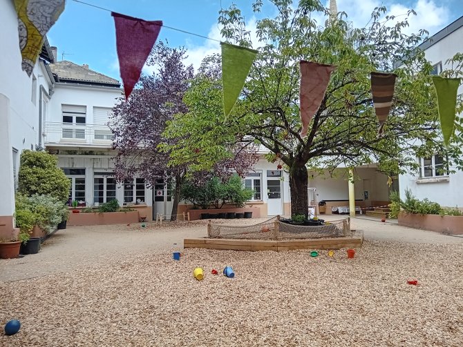 Cours buissonnières un arbre au centre les batiments au fond