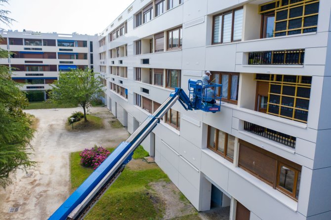 Visuel d'un immeuble en rénovation avec 2 agents sur une grue bleue