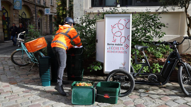 Une bornes mobile à déchets alimentaires installée dans une rue pavée de Bordeaux tirée par un vélo