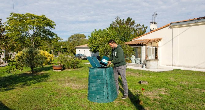 Une personne est en train de vider ses déchets alimentaires dans son composteur dans son jardin